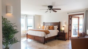 A spacious bedroom with a large bed, a ceiling fan, a nightstand with a lamp, and a view of the outdoors through a sliding glass door.