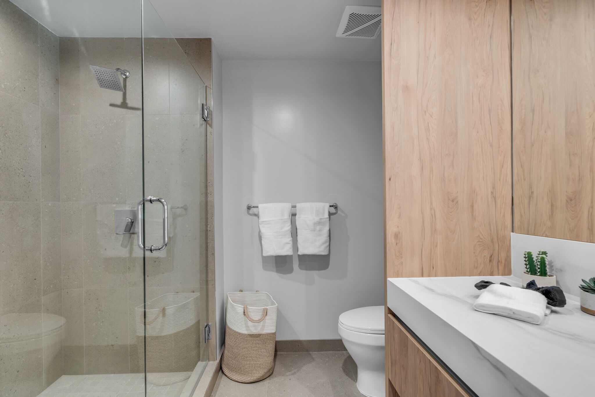 A modern bathroom with a glass-enclosed shower, a toilet, and a wooden vanity with a marble countertop.