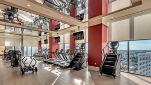 Een moderne sportschool met loopbanden, elliptische trainers en gewichtstoestellen, grote ramen met uitzicht op de stad, en een hoge ruimte met zichtbare balken.