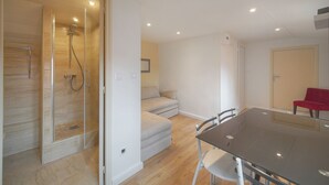 A modern room with a glass shower enclosure, a sofa, a dining table with chairs, and a red chair. - Cannes hyper center historic district of suquet-palais du festival - Croisette (Cannes)