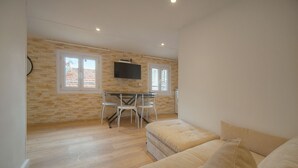 A modern living room with a wooden floor, a beige sofa, a dining table with chairs, and a TV mounted on the wall. - Cannes hyper center historic district of suquet-palais du festival - Croisette (Cannes)