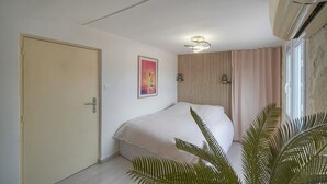 A bedroom with a bed, a door, a wall-mounted light fixture, a poster, and a window with curtains. - Cannes hyper center historic district of suquet-palais du festival - Croisette (Cannes)