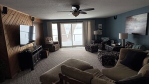 A living room with a ceiling fan, a large window, and a couch with a pillow labeled 'ON LAKE TIME'. - Lake home with beautiful views, private sandy beach, great location. (Alexandria)