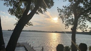 A lakeside view with a dock extending into the water, surrounded by trees. - Lake home with beautiful views, private sandy beach, great location. (Alexandria)