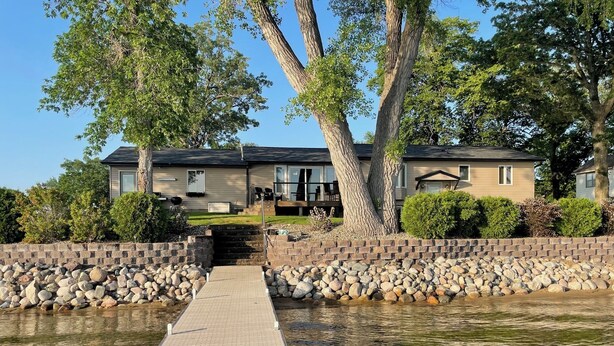 A wooden dock leading to a house with a stone wall and trees. - Lake home with beautiful views, private sandy beach, great location. (Alexandria)