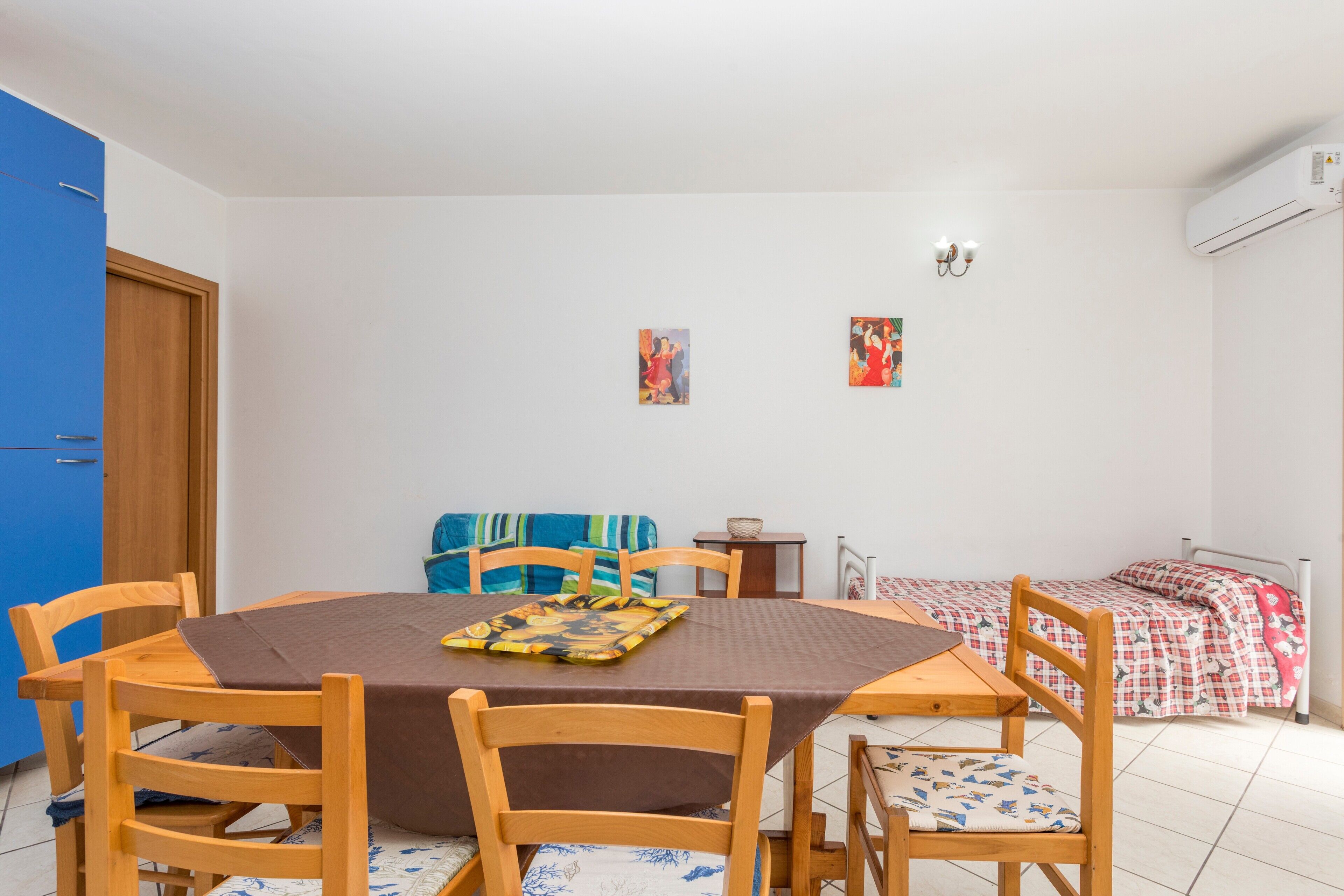 Une pièce comprenant une table à manger, des chaises, un canapé, un lit et deux œuvres d’art accrochées au mur.