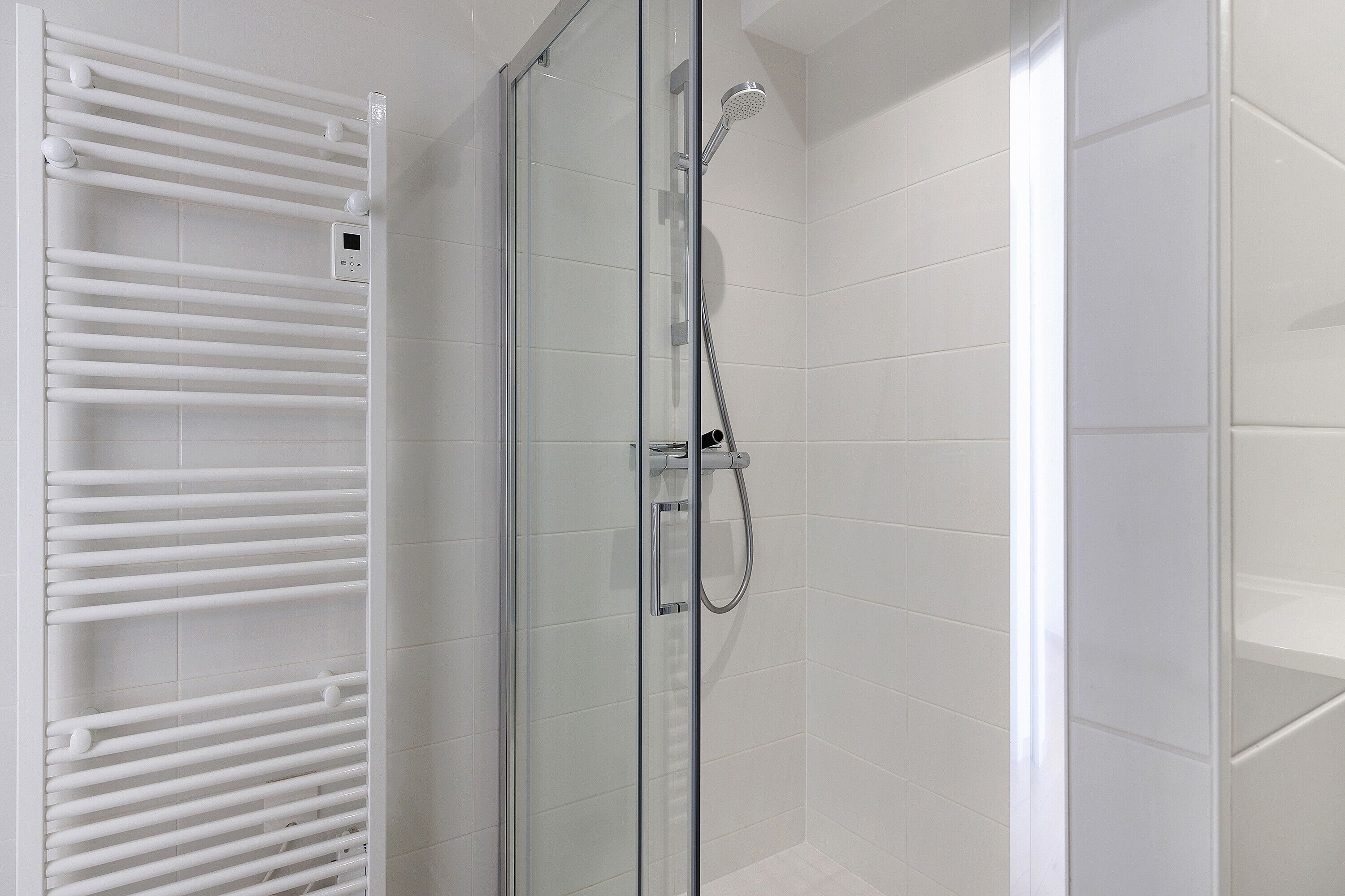 A glass-enclosed shower with a handheld showerhead and a control panel.