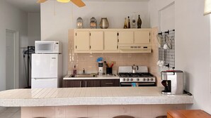 A kitchen with a ceiling fan, white cabinets, a microwave, a stove, and three stools. - Sun bathed studio apartment with mountain views just minutes from the beach! (Rincón)