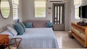 A bedroom with a bed, a wooden dresser, a ceiling fan, and a TV. - Sun bathed studio apartment with mountain views just minutes from the beach! (Rincón)