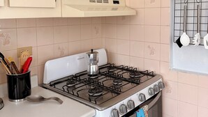 A kitchen with a stove, cabinets, and a window with kitchen utensils hanging. - Sun bathed studio apartment with mountain views just minutes from the beach! (Rincón)