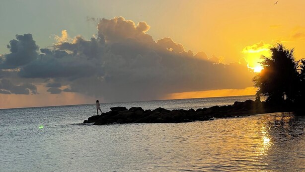 A beach scene with a sunset, calm water, and a rocky outcrop. - Sun bathed studio apartment with mountain views just minutes from the beach! (Rincón)