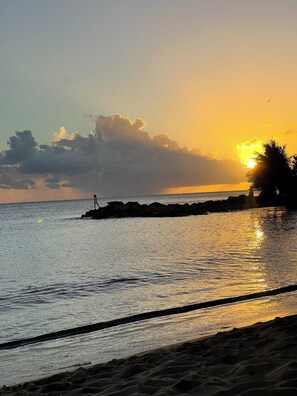 A beach scene with a sunset, calm water, and a rocky outcrop. - Sun bathed studio apartment with mountain views just minutes from the beach! (Rincón)