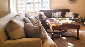 A living room with a large window, a round wall clock, and a coffee table with books. - 3BR/3BA Pet-Friendly, 2 Blocks to Beach, Walk to Dining & Coffee (Seal Beach)