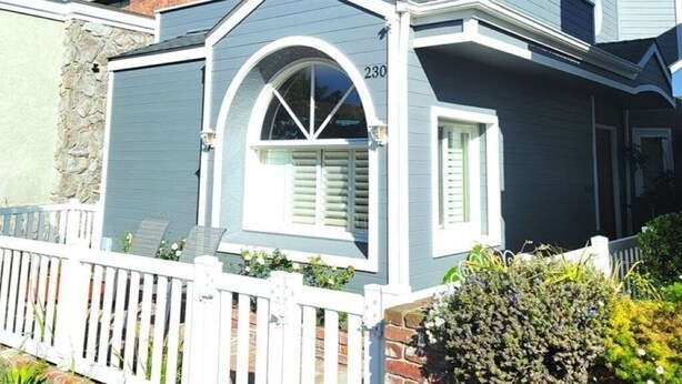 A two-story house with a blue exterior, a brick chimney, and a white picket fence. - 3BR/3BA Pet-Friendly, 2 Blocks to Beach, Walk to Dining & Coffee (Seal Beach)
