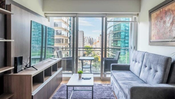 Ein modernes Wohnzimmer mit einer Couch, einem Couchtisch, einem Fernseher und einem Balkon mit Blick auf die Stadt.