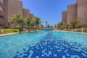 A swimming pool with blue mosaic tiles, surrounded by palm trees and a brick building. - Scopa Beach #c3-200 - Beachfront By Carpediem (Aquiraz)