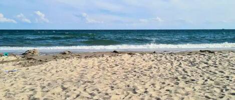 A sandy beach with visible footprints and a calm sea under a clear sky.