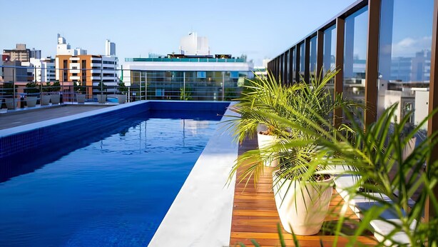 A rooftop pool with a wooden deck and potted plants, overlooking a cityscape with modern buildings. - Buenos Ayres #509 - Apt With Balcony by Carpediem (João Pessoa)