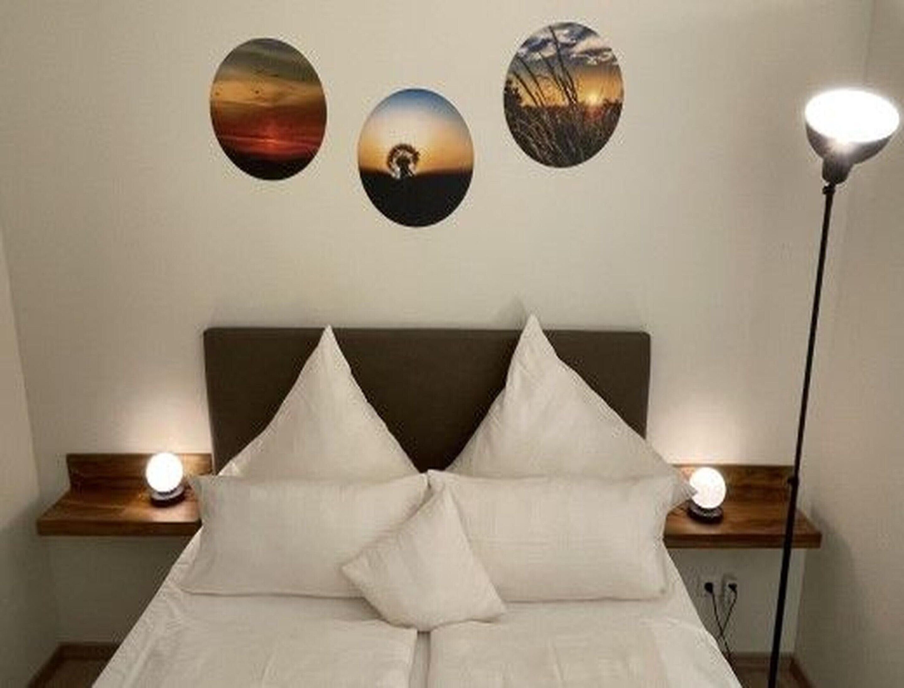 A neatly made bed with two pillows, a bedside table with a lamp, and three framed pictures on the wall.