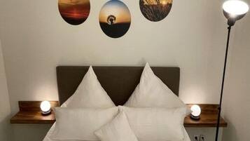 A neatly made bed with two pillows, a bedside table with a lamp, and three framed pictures on the wall.