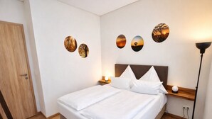 A neatly made bed with white linens, a wooden headboard, and a bedside table with a lamp. There are three wall-mounted decorative plates above the bed. - Bernsteinsee Homes and Ferien Beach House (Sassenburg)