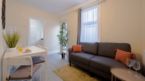 A modern living room with a sofa, a dining table with chairs, a small coffee table, and a potted plant. - 2-bedroom Bright London Home (London)