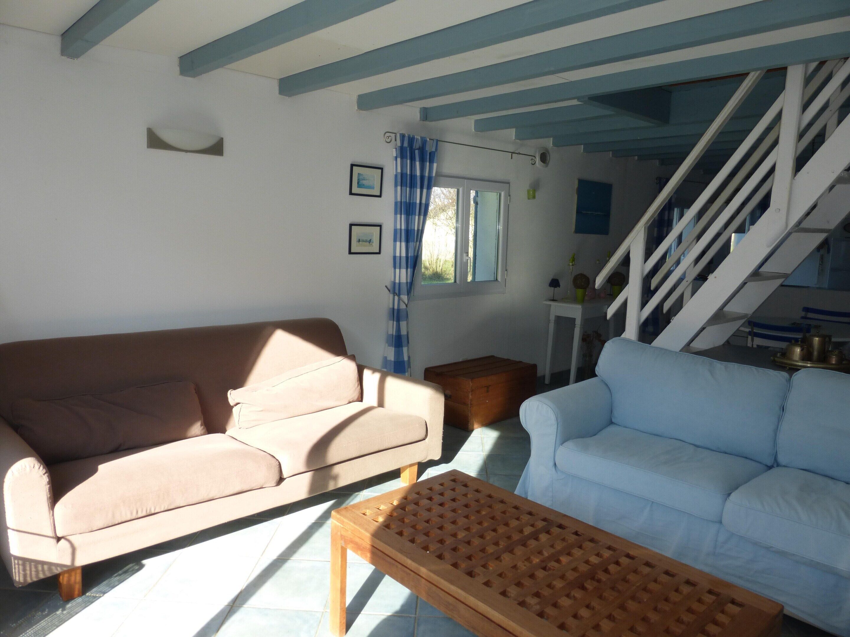 Un salon avec un canapé beige, un canapé bleu clair et une table basse en bois. Un escalier mène à un niveau supérieur.