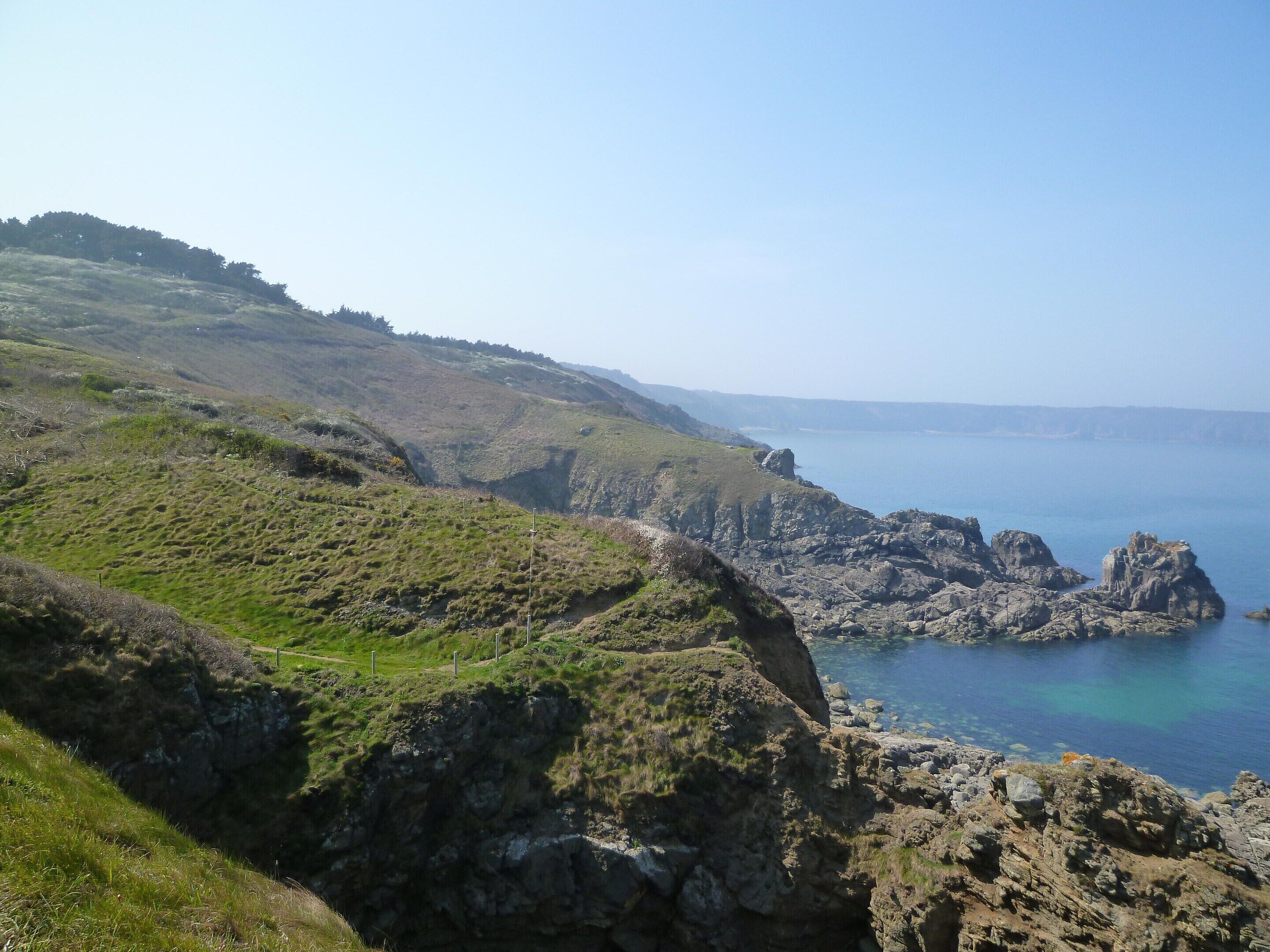 A coastal landscape with rocky cliffs and a clear view of the sea.