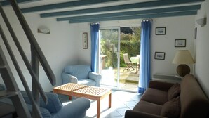 A living room with a blue armchair, a brown sofa, a wooden coffee table, and a dining area with a table and chairs. - Cosy House Just Steps Away From the sea (Lamballe-Armor)