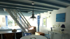 A dining area with a round table, blue chairs, a staircase, and a window with curtains. - Cosy House Just Steps Away From the sea (Lamballe-Armor)