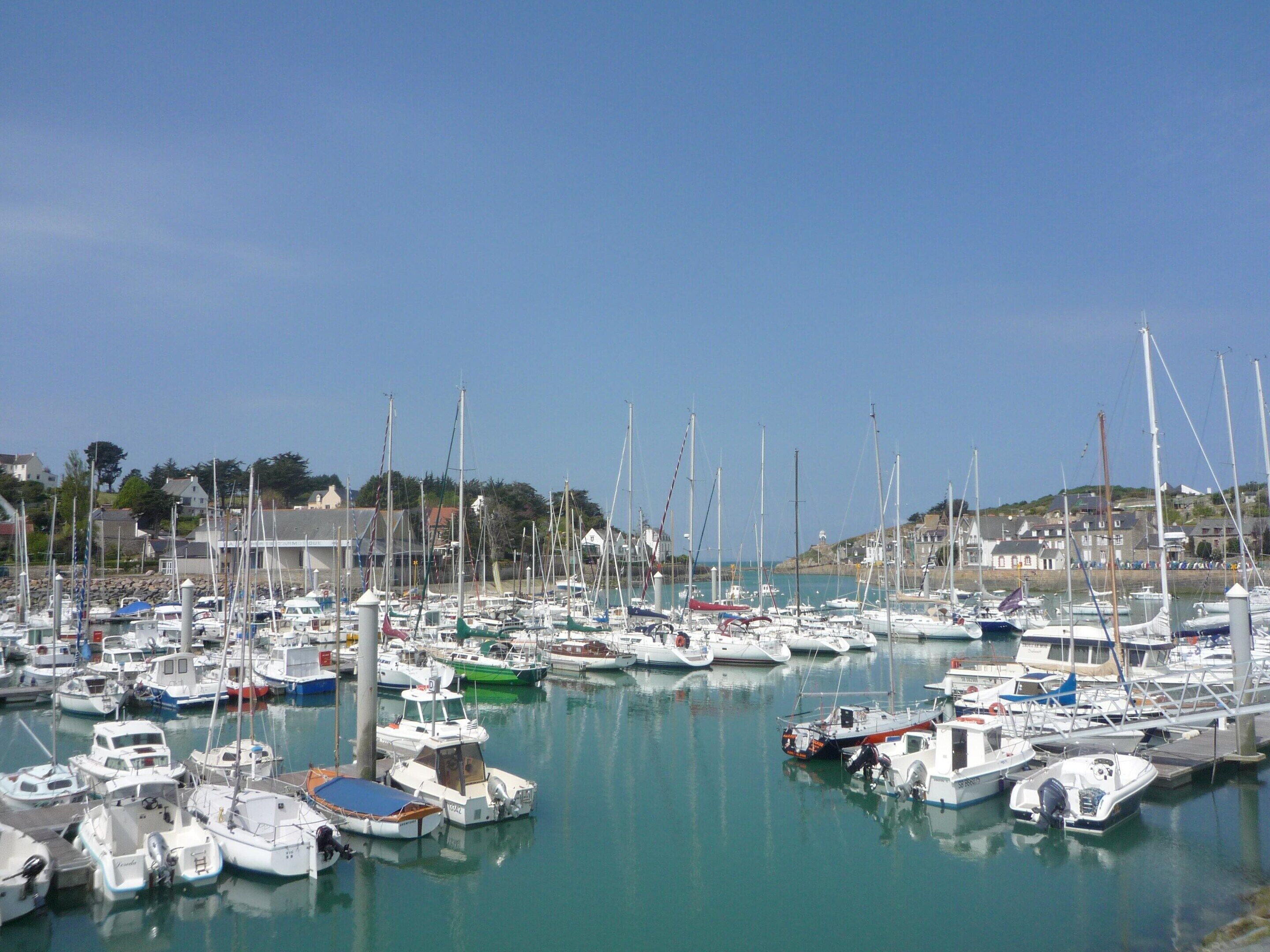 A marina with various boats docked, surrounded by buildings and hills in the background.