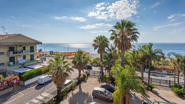 Un quartier résidentiel situé sur la côte, avec vue sur la mer, des voitures garées et des palmiers.