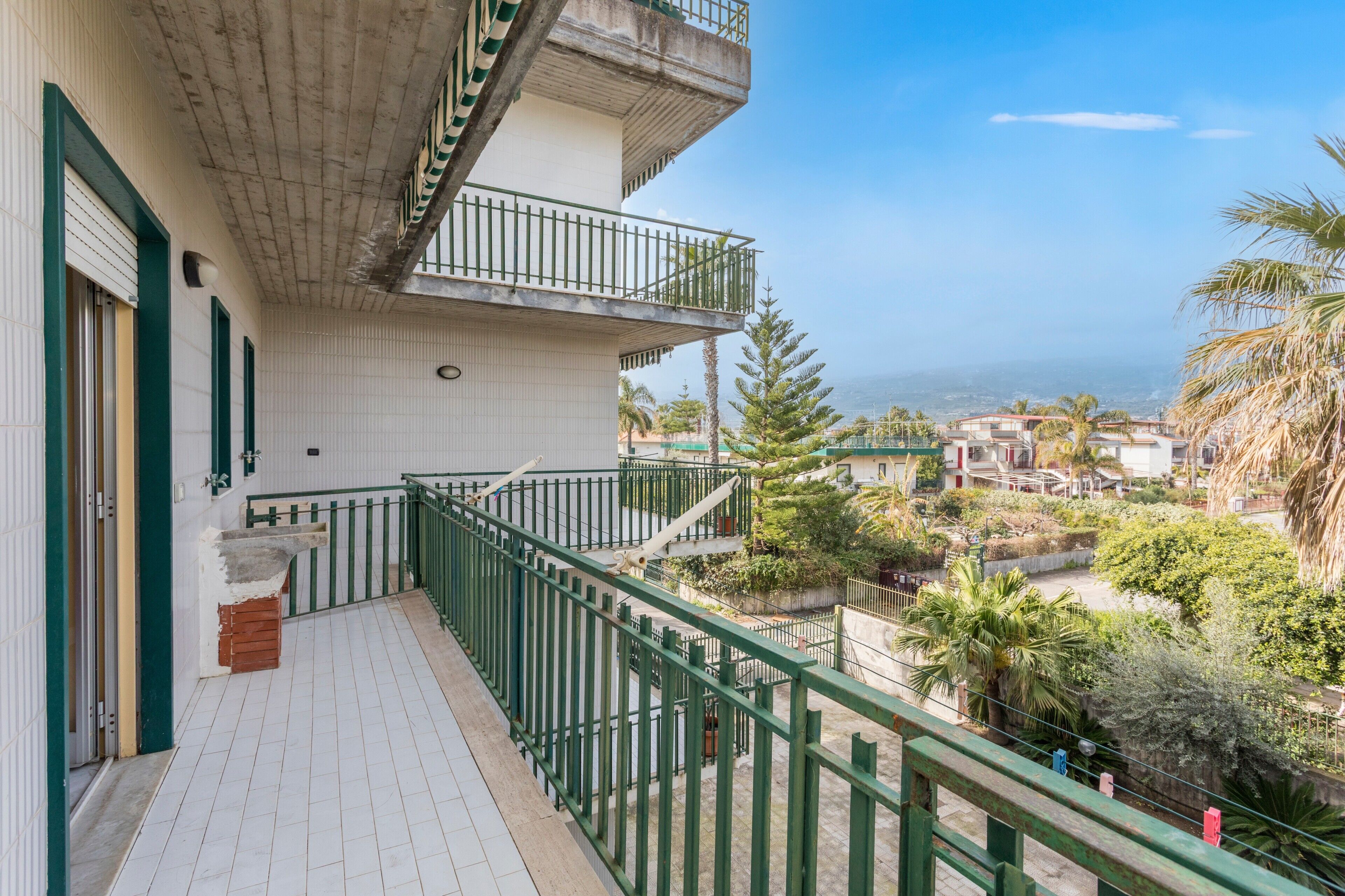 A balcony with a green railing overlooking a residential area with houses and trees.