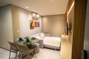 Une chambre d’hôtel de taille réduite, comprenant un lit, une petite table à manger avec des chaises, un canapé et un climatiseur fixé au mur.