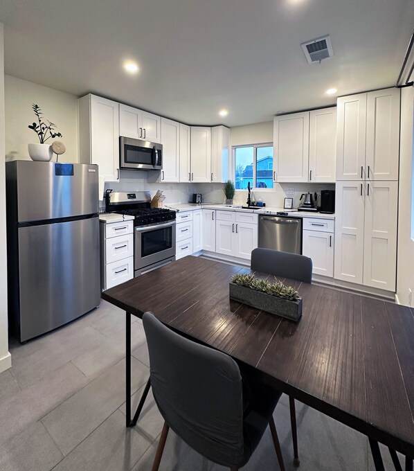 Una cocina moderna con armarios blancos, electrodomésticos de acero inoxidable y una mesa de comedor de madera oscura.