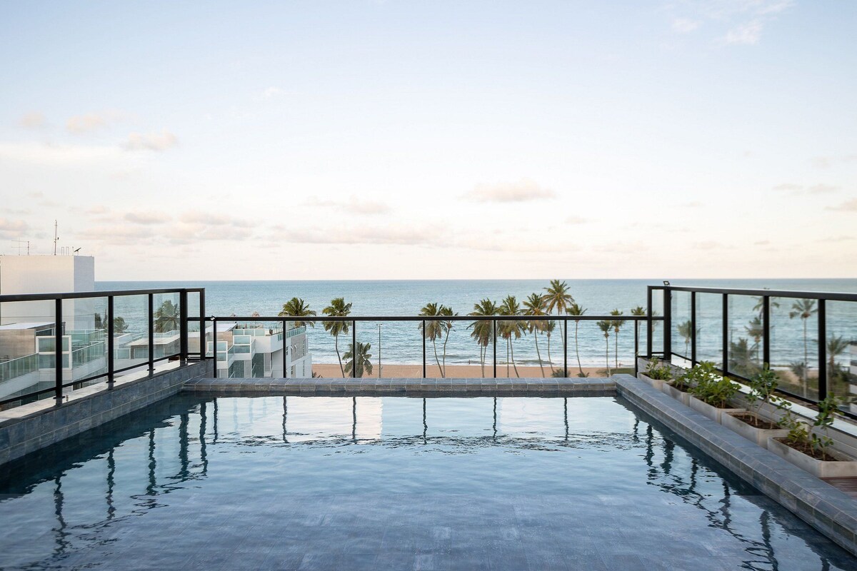 An infinity pool with a view of the beach and palm trees.