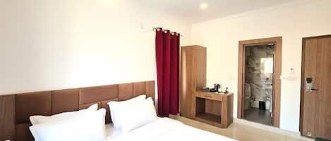 A hotel room with a large bed, a wooden wardrobe, a desk with a chair, and a bathroom visible through an open door.