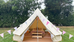 A large, triangular tent with a bed and seating area inside, surrounded by a grassy field and trees. - Dovedale (Ashbourne)