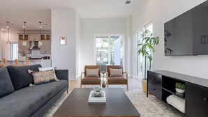 Een moderne woonkamer met een donkere salontafel, twee fauteuils, een bank en een televisie aan de muur.