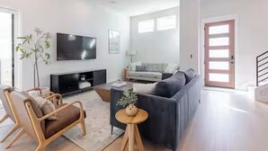 Een moderne woonkamer met een bank, een televisie, een plant en een houten salontafel.