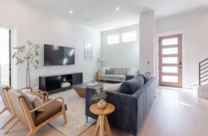 Ein modernes Wohnzimmer mit einer Couch, einem Fernseher, einer Pflanze und einem Holztisch.