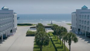 A modern hotel with a central courtyard, palm trees, and a view of the ocean. - Casa Del Mar 272-seashells & Tail Fins (Galveston)