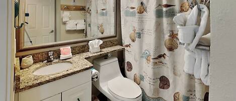A bathroom with a sink, mirror, toilet, and shower curtain with sea creature designs.