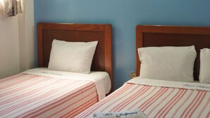 Een hotelkamer met twee bedden, een plafondventilator en een lamp aan de muur.