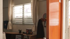 Een kamer met een houten bureau, een computer, een raam met gordijnen en een deur.