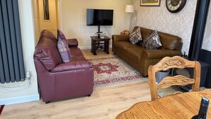 A living room with a brown sofa, a red sofa, a wooden coffee table, a television, and a fireplace. - Blakelaw Court (Alnwick)