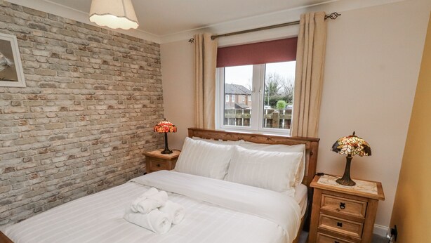 A neatly made bed with white linens and a rolled towel, a wooden headboard, a brick wall, and two bedside tables with lamps. - Blakelaw Court (Alnwick)