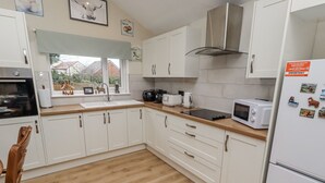 A modern kitchen with white cabinets, a stainless steel range hood, a microwave, and a refrigerator. - Blakelaw Court (Alnwick)
