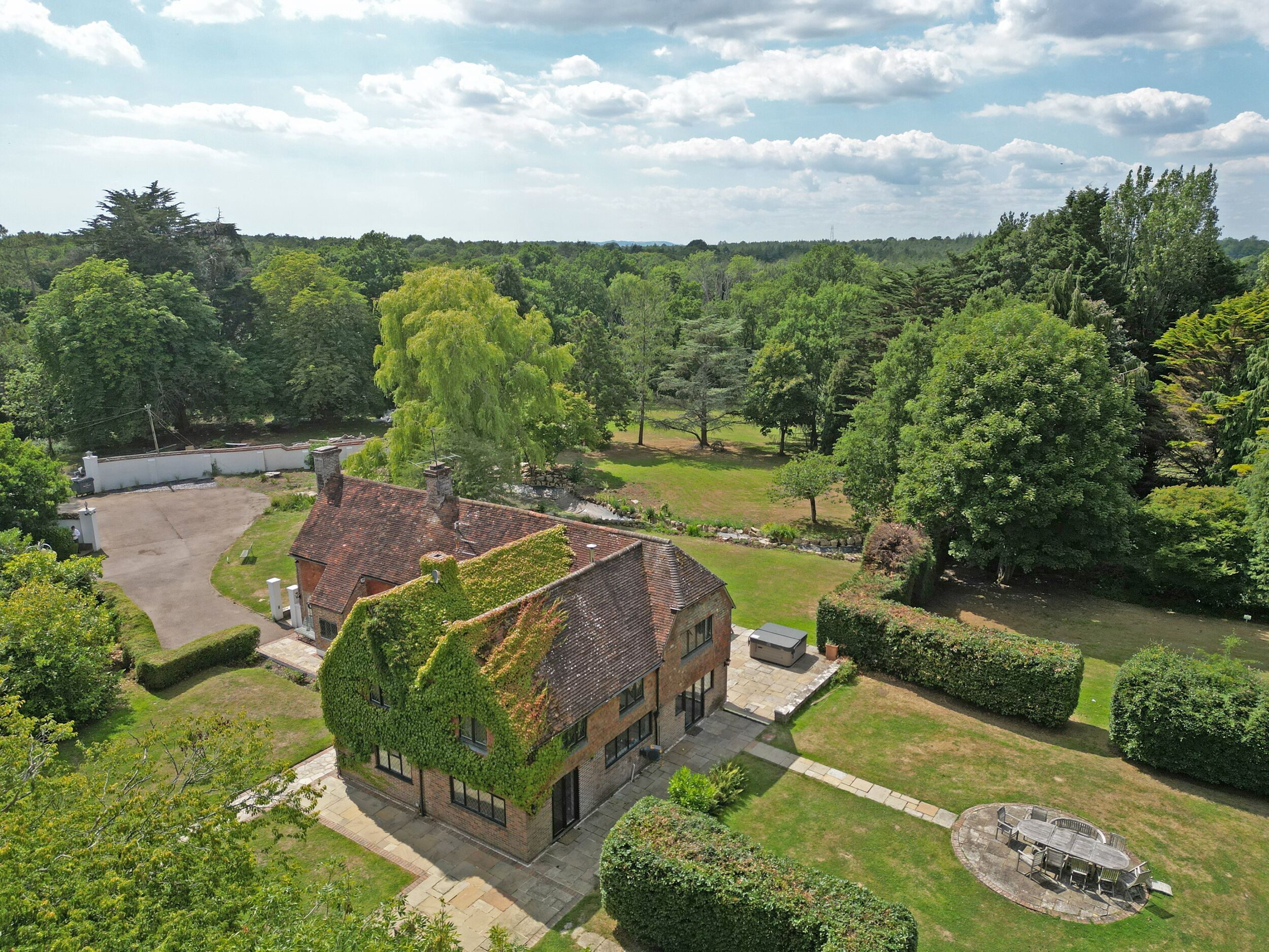 A house with a brick exterior and ivy-covered roof, surrounded by a well-maintained garden and a small pond.