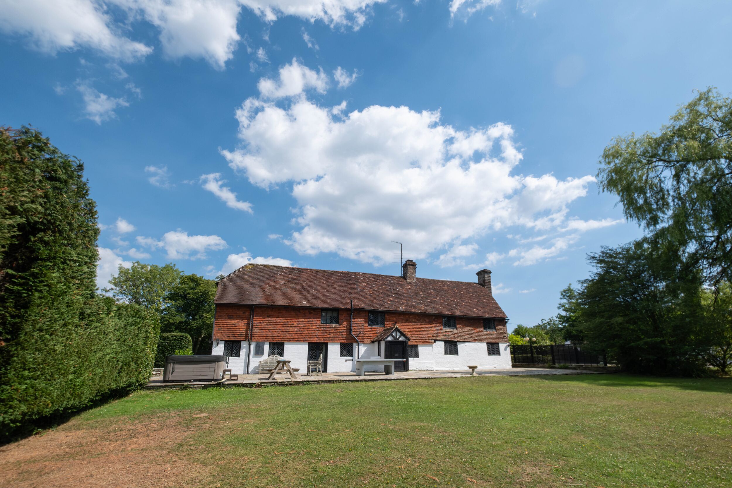 A traditional two-story house with a sloped roof and a chimney, surrounded by a well-maintained lawn and mature trees.